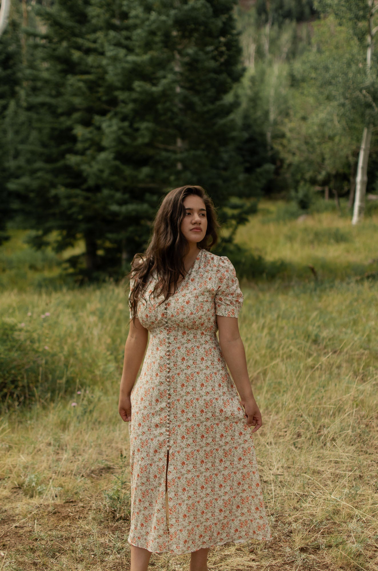 Woman in the woods wearing a floral dress, cream with peach roses , V-neckline, front button detail following a slit.