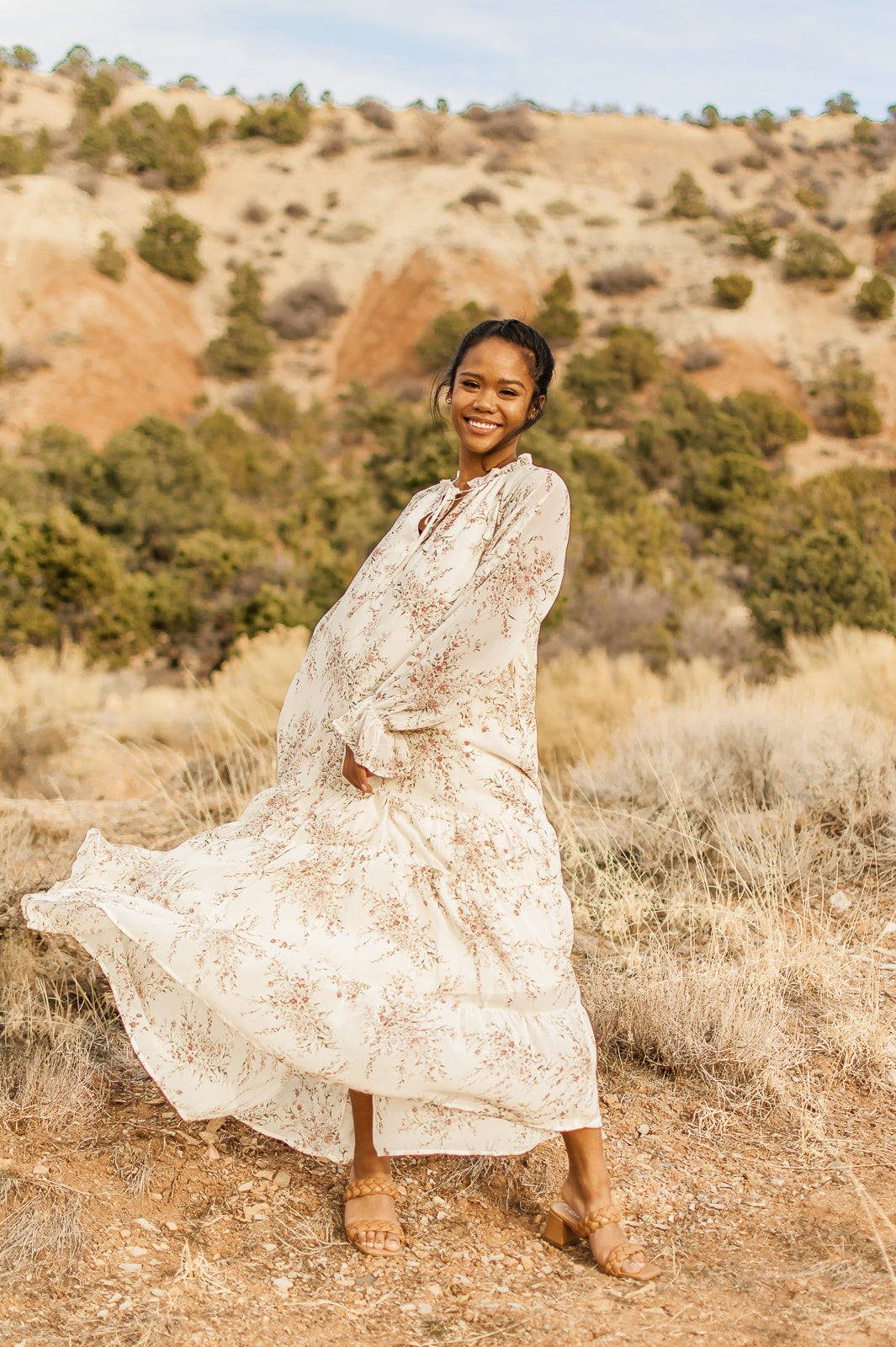 Women displaying a elegant flowy, floral, cream, boho style maxi dress, lined, V-neck with straps, bell cuff sleeves, and tiered bottom. bella by grace co.