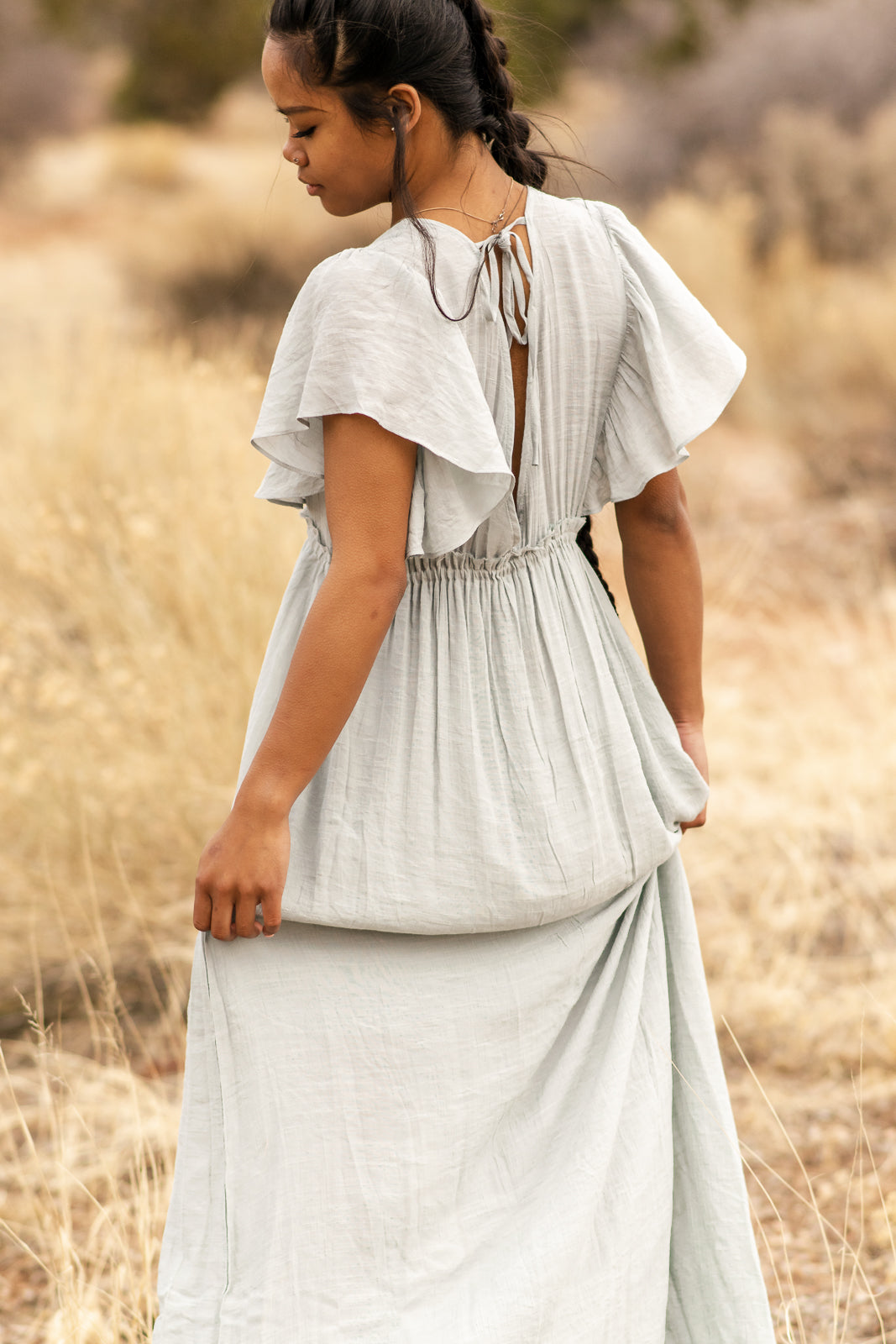 Women modeling back of light blue dress with adjustable back laces in the back with angle sleeves. bella by grace co. 